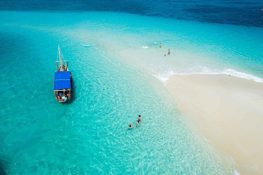 A boat on turquoise water near a sandy beach with people swimming. 1