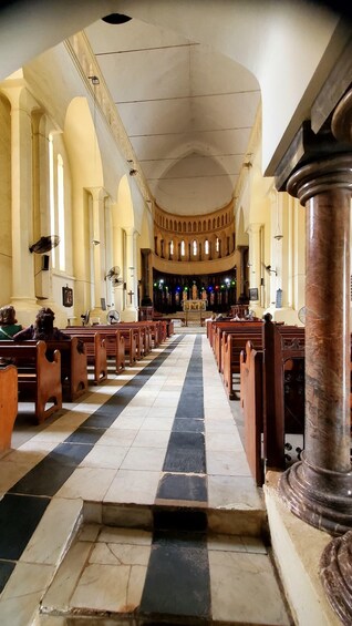 An interior of a church with rows of wooden pews, a central aisle leading to an altar, and a vaulted ceiling. 1