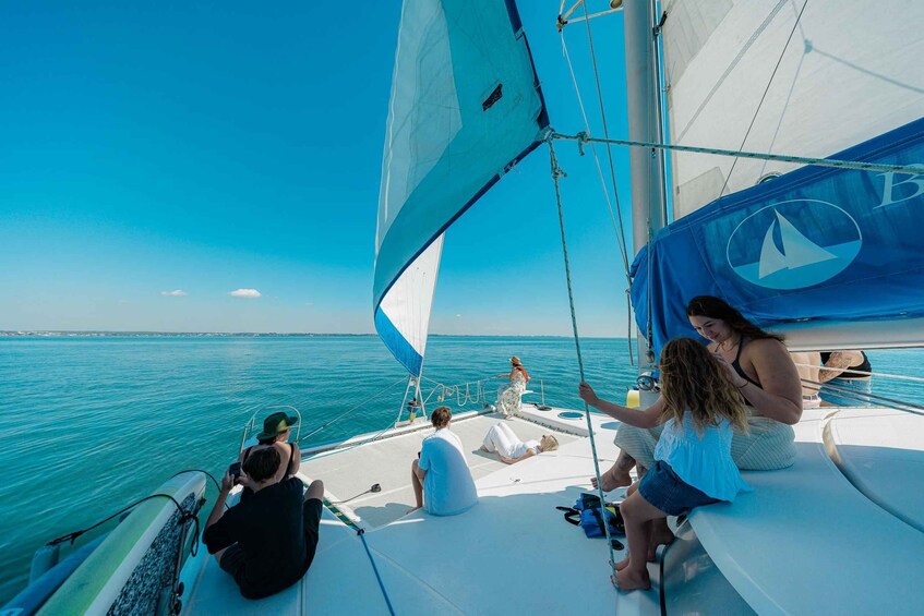 A sailboat with people on deck, a clear blue sky, and calm sea. 3