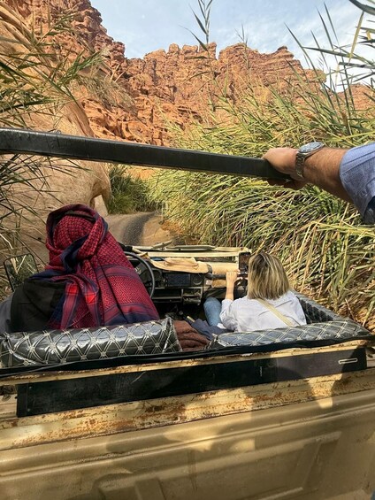 A vehicle with two passengers, one holding a camera, driving through a canyon with red rock formations. 4