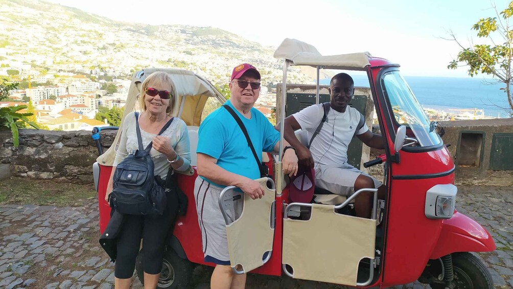 Three people on a red three-wheeled vehicle with a scenic coastal background. 3