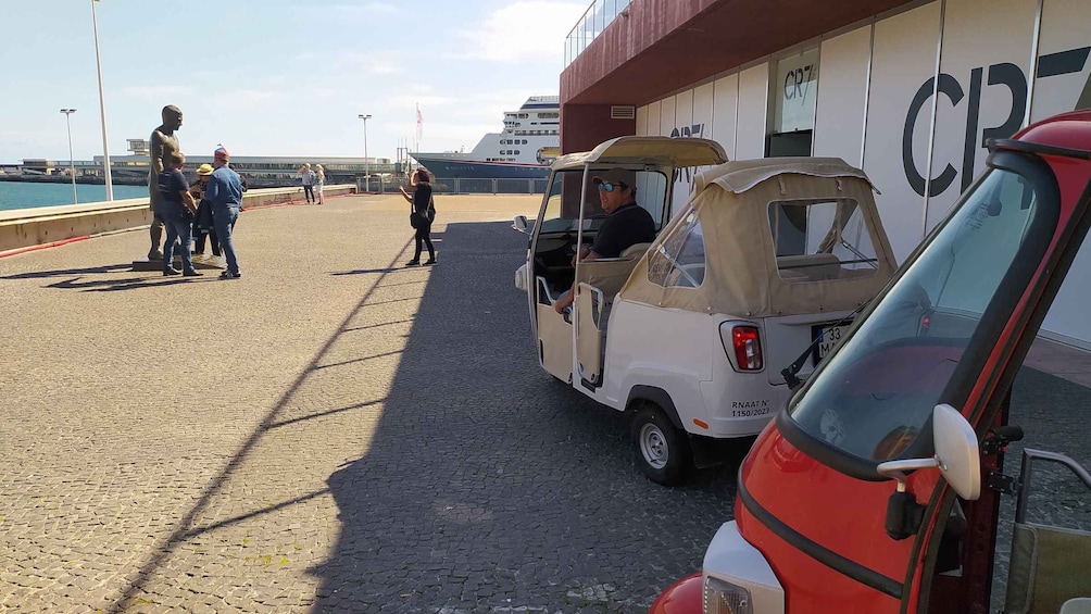 A coastal area with a statue, a small vehicle, and a large ship in the background. 1