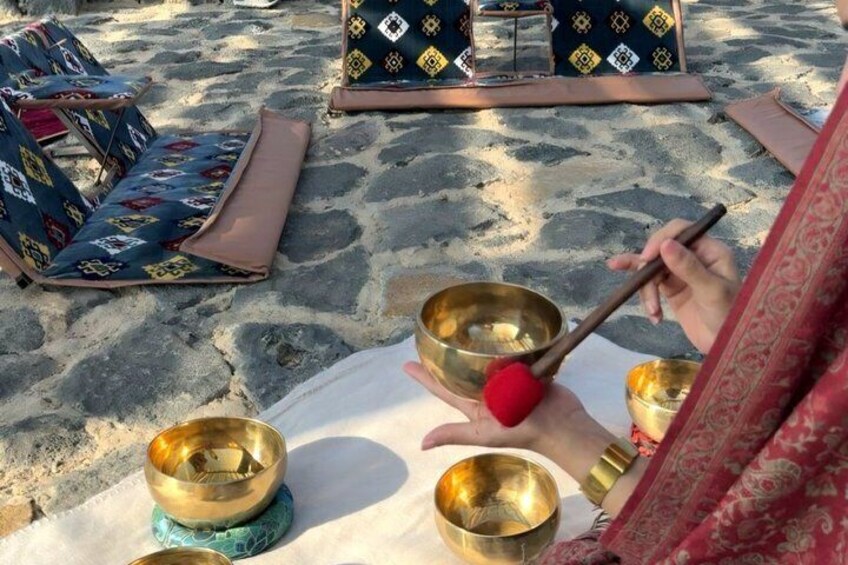 A person playing a handpan outdoors with several other handpans and cushions on the ground. 4