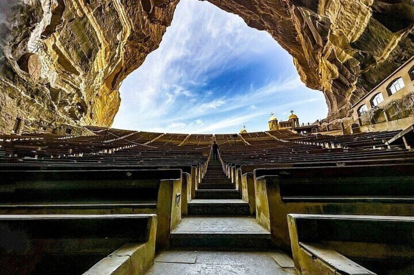 An empty amphitheater with steps leading to a central stage, framed by rock formations. 1