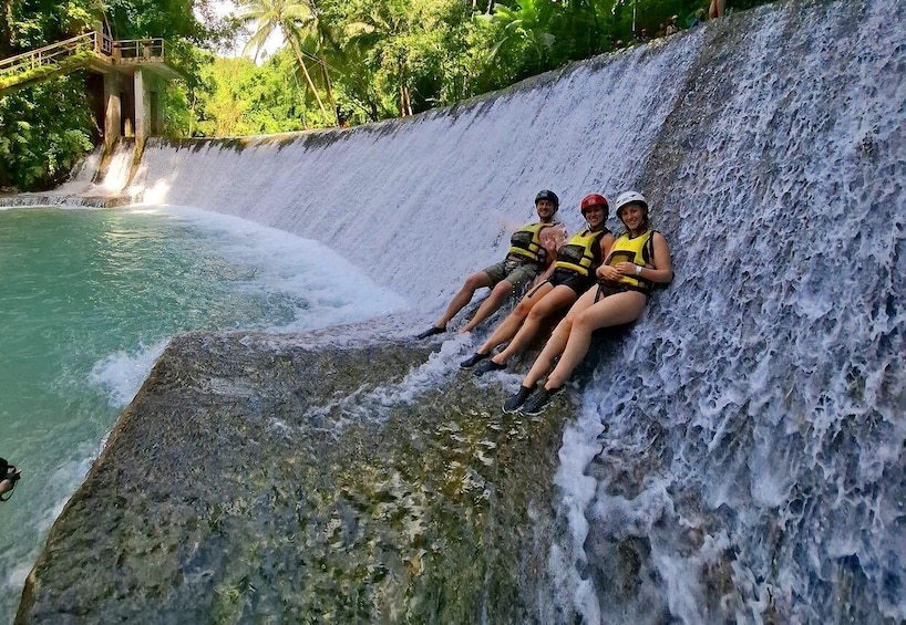 A waterfall with people sitting on a rock ledge. 5