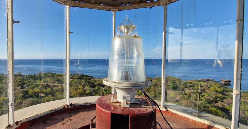 A lighthouse on a rocky outcrop with a view of the ocean and a distant bridge. 2
