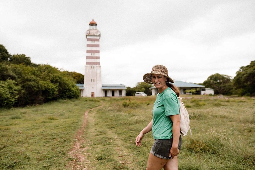 A person walking on a grassy path with a lighthouse in the background. 1