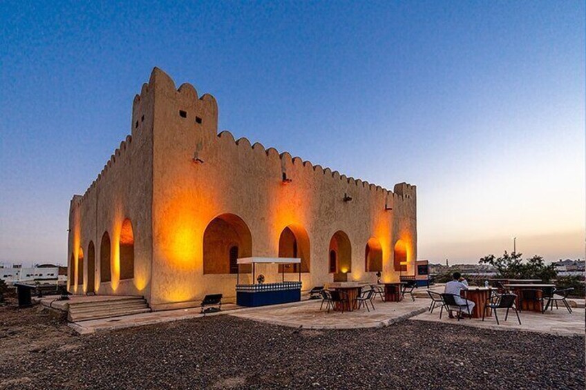 A historic building with arched windows and a tower, illuminated by warm lights. 1