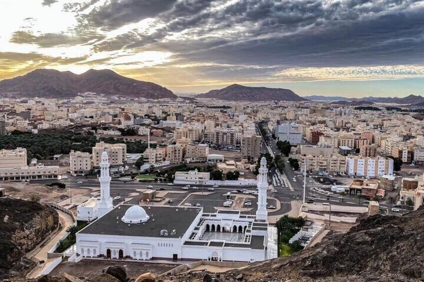 A cityscape with a prominent mosque featuring two minarets and a dome, surrounded by residential buildings and mountains in the background. 3