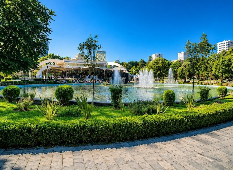 A park with a fountain, neatly trimmed hedges, and a modern building with a dome. 5