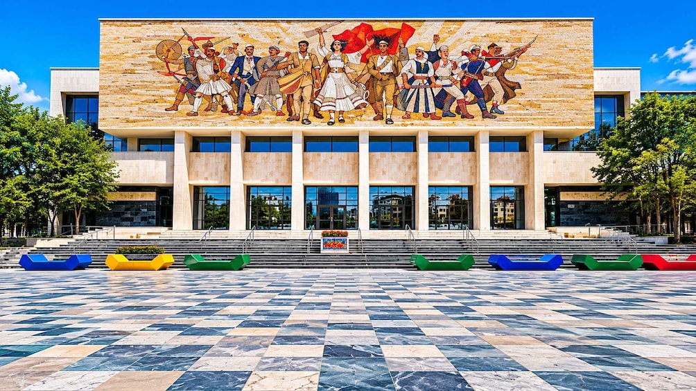 A modern building with a mosaic mural of historical figures and colorful boats in front. 4