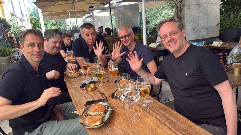 A group of people sitting at an outdoor table with drinks and sandwiches. 3