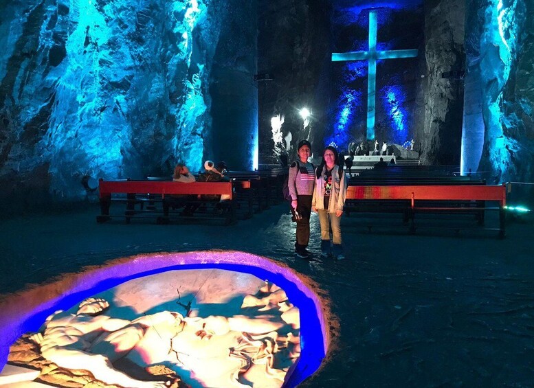 A cave with illuminated blue lighting and a large cross. There are benches and a pool of water with fish. 5