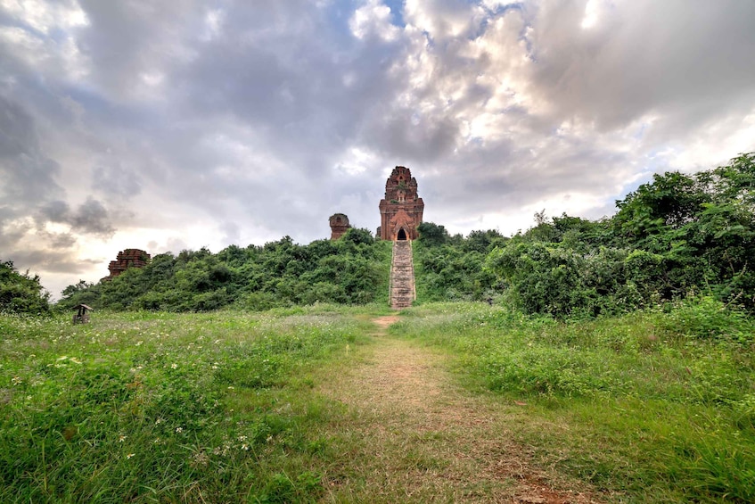 Un sendero conduce a una alta estructura de piedra antigua, rodeada de vegetación exuberante y un cielo nublado. 5