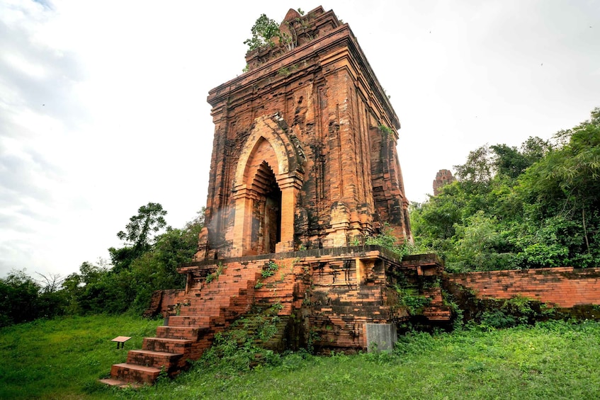 Un antiguo templo de ladrillo con un arco central y una escalera que conduce a él, rodeado de exuberante vegetación. 3