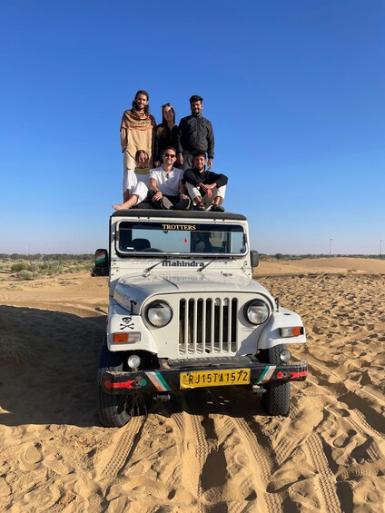 A white Mahindra Trotters vehicle with four passengers on a sandy desert road. 5