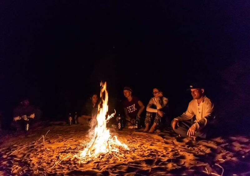 A group of people sitting around a campfire on a sandy beach at night. 3