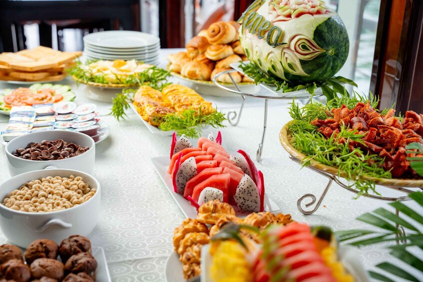 A buffet with various food items including a watermelon carved into a face, pastries, and a selection of fruits and nuts. 3