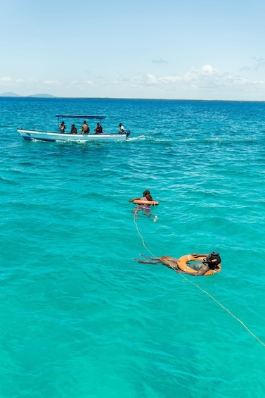 A boat with people on a turquoise sea, a person swimming with a rope, and another person on a float. 4