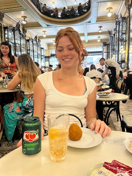 A woman sitting at a table in a restaurant with a can of Guarana Antarctica Zero and a glass of juice. 5
