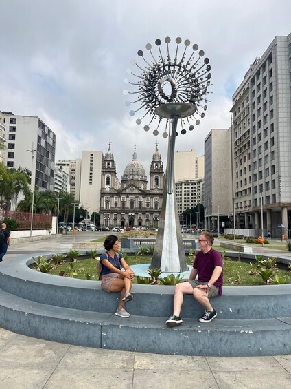 A sculpture in a plaza with a historic building in the background. 1