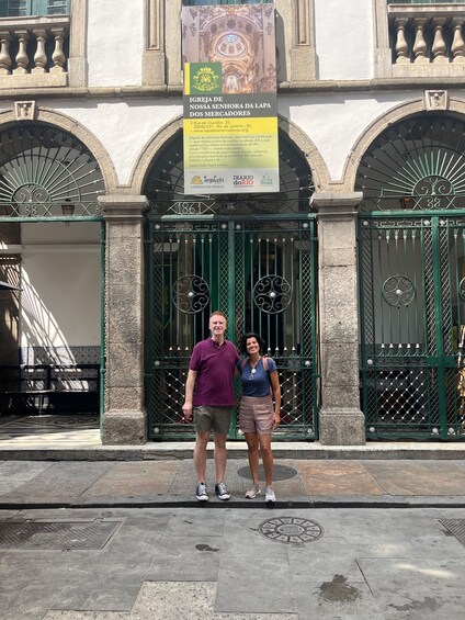 A couple standing in front of a historic building with ornate gates and a banner. 4