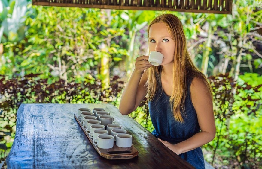 Una persona sentada en una mesa de madera al aire libre, con una bandeja de tazas blancas. 4