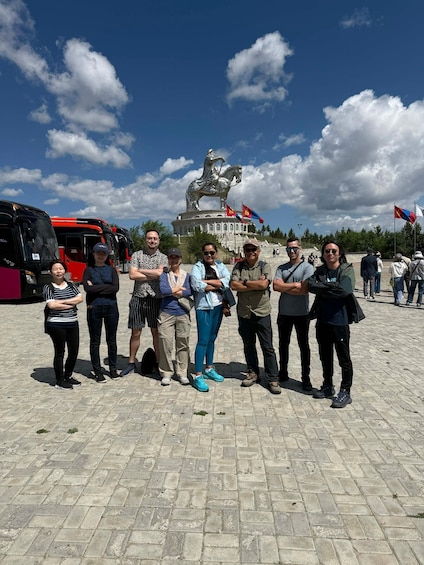 A group of people standing in front of a statue with flags, with buses in the background. 5