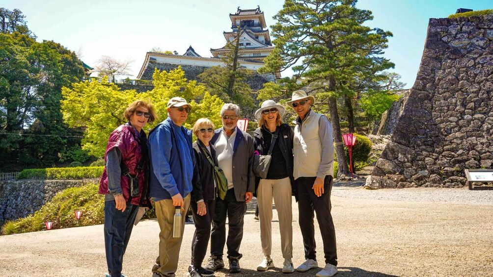 A group of people standing in front of a traditional Japanese castle with a stone wall and trees in the background. 3