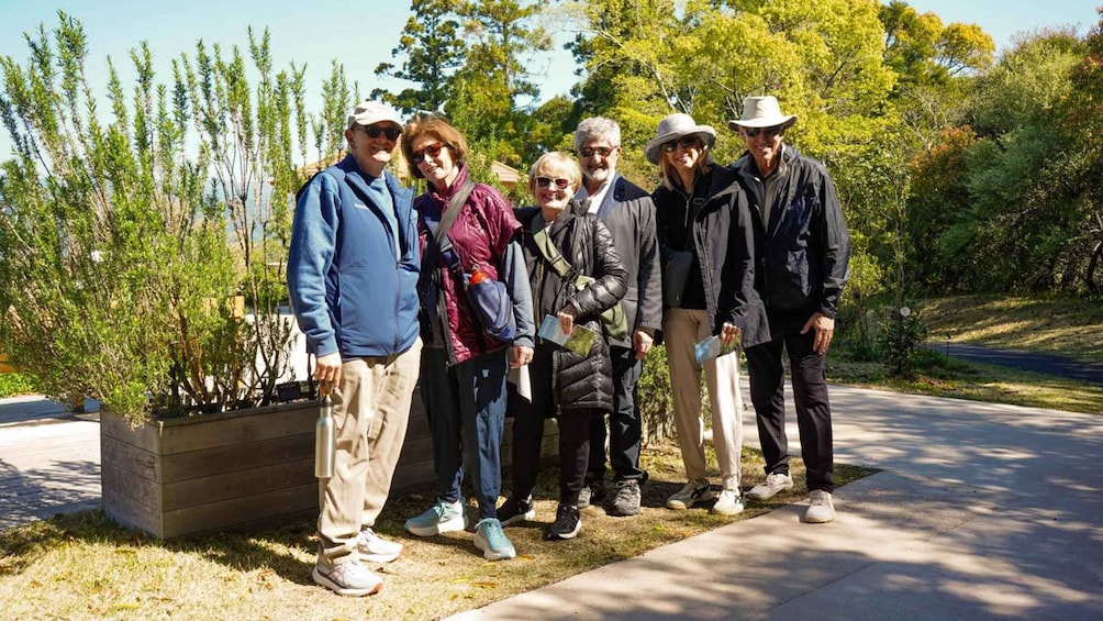 A group of people standing outdoors in a park with trees and a paved path. 5