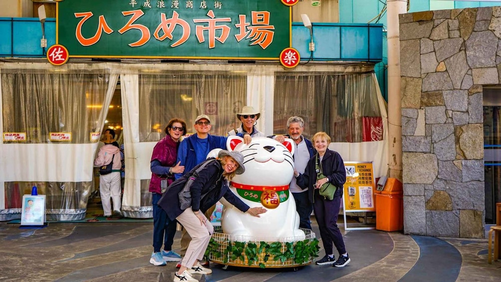A group of people posing in front of a shop with a large cat statue. 4