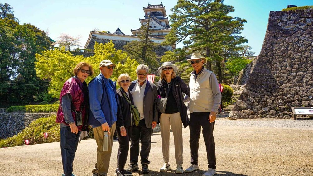 A group of people standing in front of a traditional Japanese castle with a stone wall and trees in the background. 1