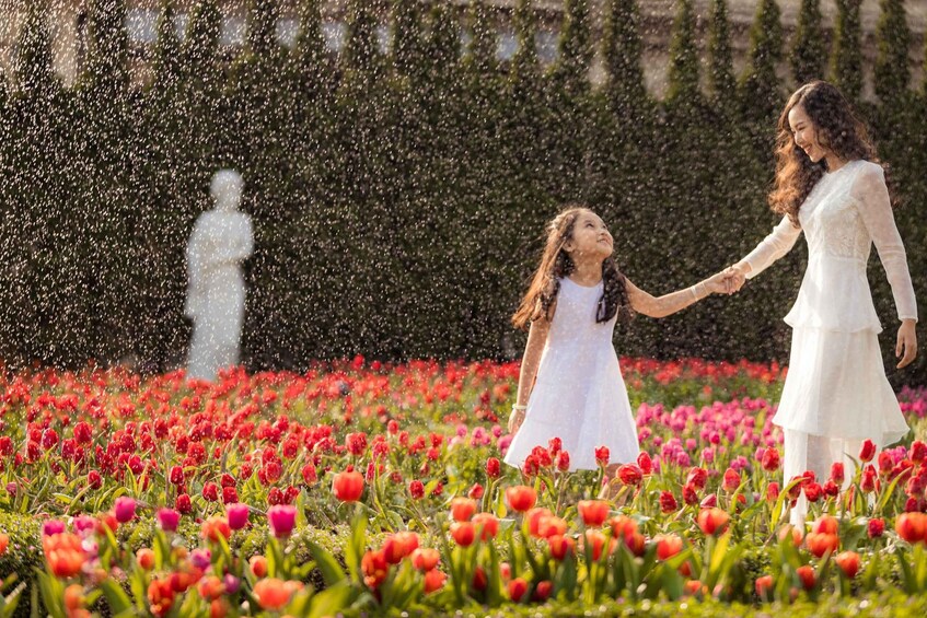 A woman and a child holding hands in a field of red tulips with a statue in the background. 2