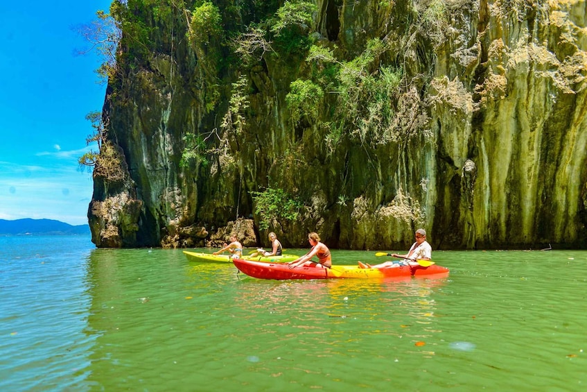 Three people kayaking on a calm river with a rocky cliff in the background. 2