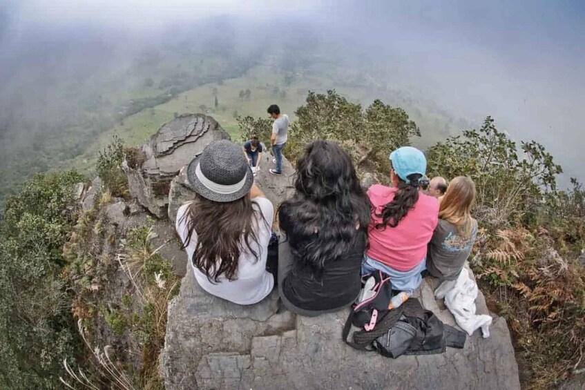 A group of people sitting on a rocky ledge overlooking a valley. 1