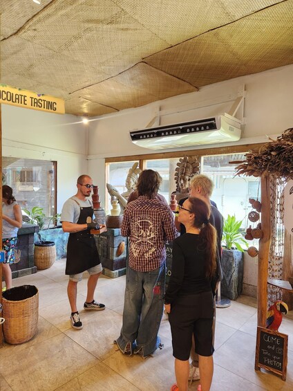 A group of people at a chocolate tasting event inside a shop with a sign reading 'CHOCOLATE TASTING'. 2