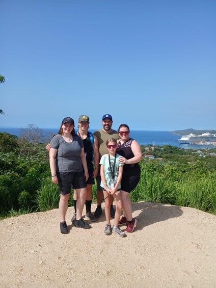 A group of people standing on a dirt path with a scenic view of the ocean and a cruise ship in the background. 1