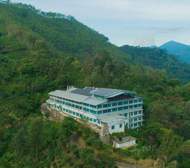 A multi-story building with solar panels on the roof, surrounded by dense forest and hills. 5