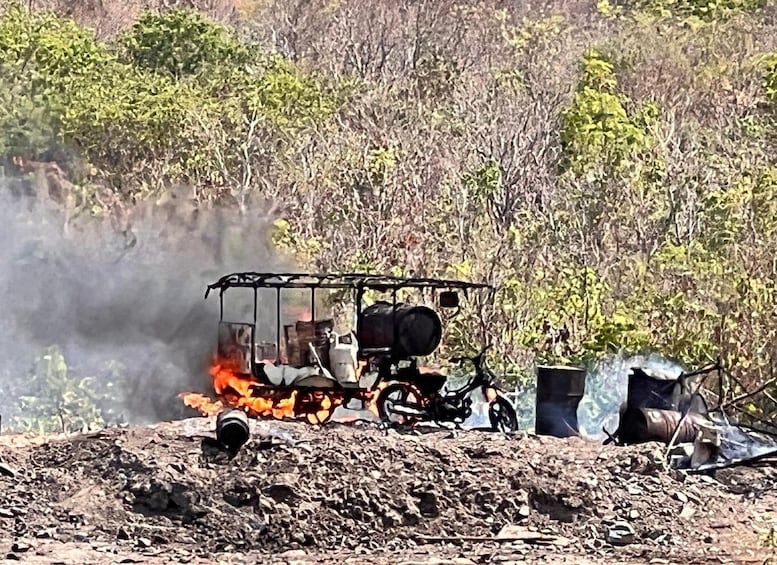 A makeshift fire pit with burning logs and a metal structure, surrounded by dry vegetation and a rocky ground. 4