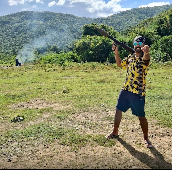 A person holding a rifle in a grassy field with hills in the background. 5