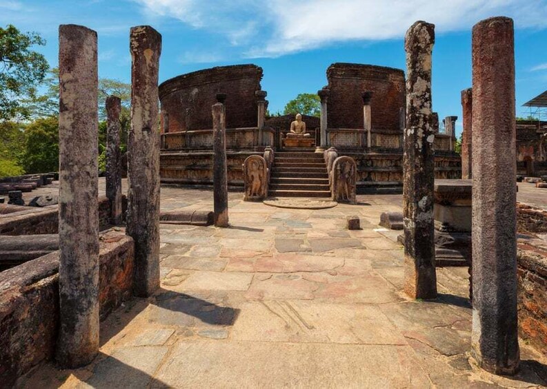 Ancient stone ruins with a central Buddha statue, surrounded by columns and steps leading to a large circular structure. 2