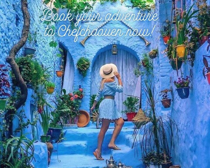 Une femme vêtue d’une robe bleue et d’un chapeau de paille se tient dans une ruelle aux murs peints en bleu, où l’on aperçoit des plantes en pot et une porte. 3