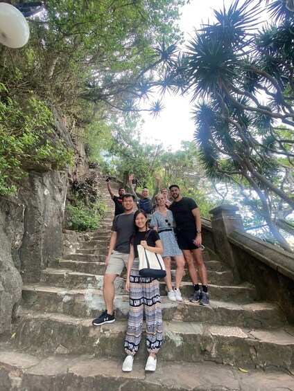 A group of people standing on stone steps surrounded by lush greenery and trees. 2