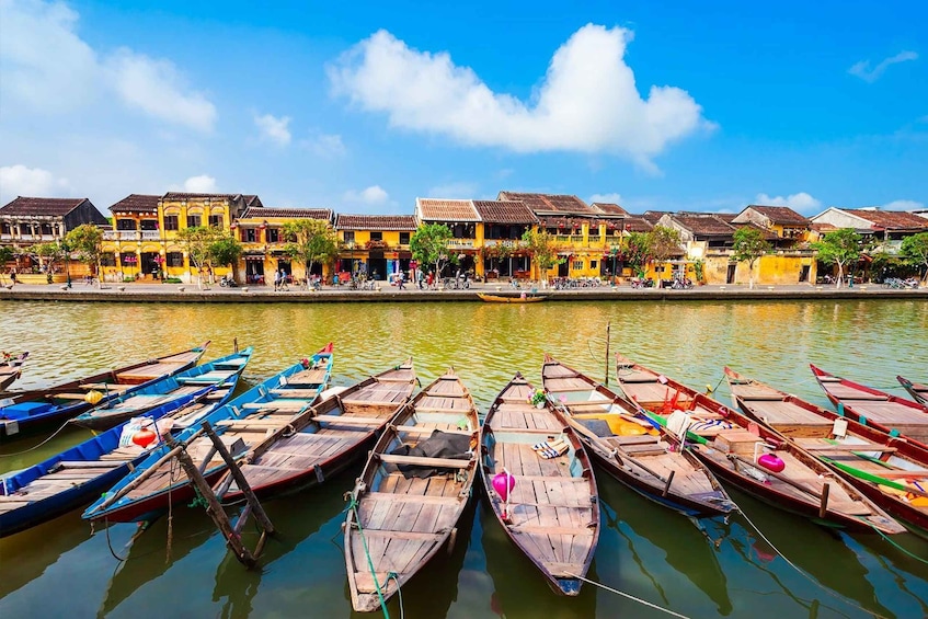 A riverside with wooden boats docked and colorful buildings in the background. 1