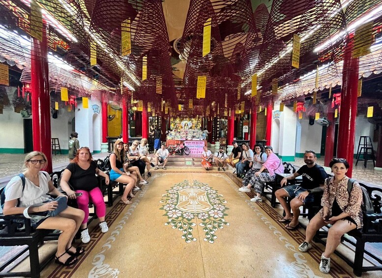A group of people seated in a temple with red pillars and a patterned floor. 3