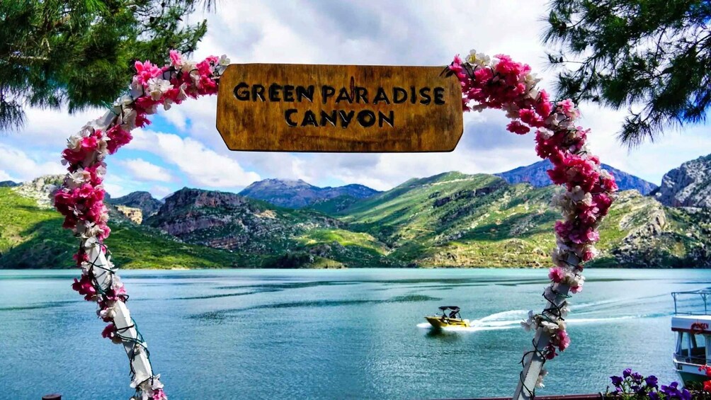A sign reading 'GREEN PARADISE CANYON' with a mountainous landscape and a body of water in the background. 3