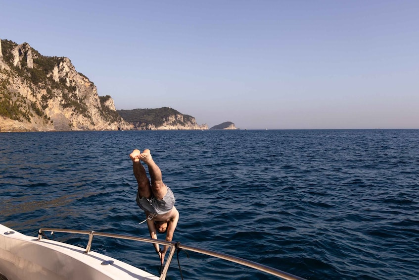 A person performing a handstand on a boat's railing over the sea with cliffs in the background. 3