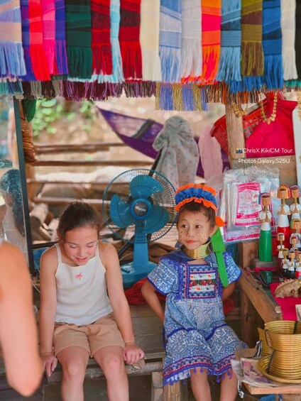 Two children sitting in a market stall with colorful fabrics and wooden toys. 1