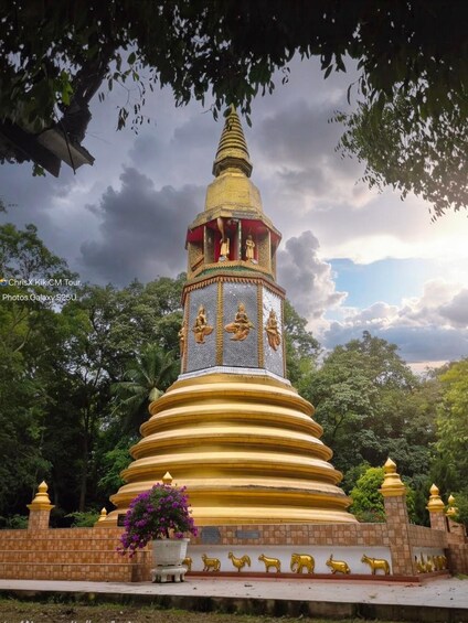 A golden stupa with intricate carvings, surrounded by lush greenery and a cloudy sky. 2