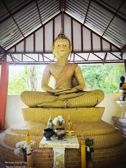 A large golden Buddha statue under a roofed structure with a brick wall and a window. 5